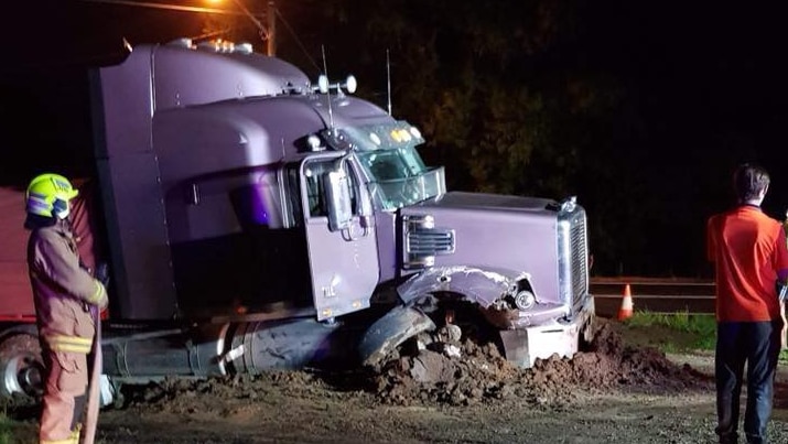 A purple truck ploughed into earth with a firefighter standing nearby.