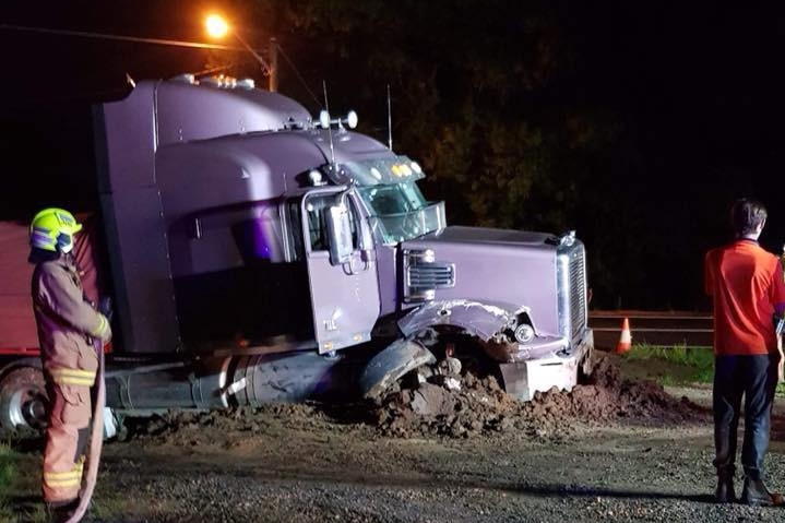A purple truck ploughed into earth with a firefighter standing nearby.