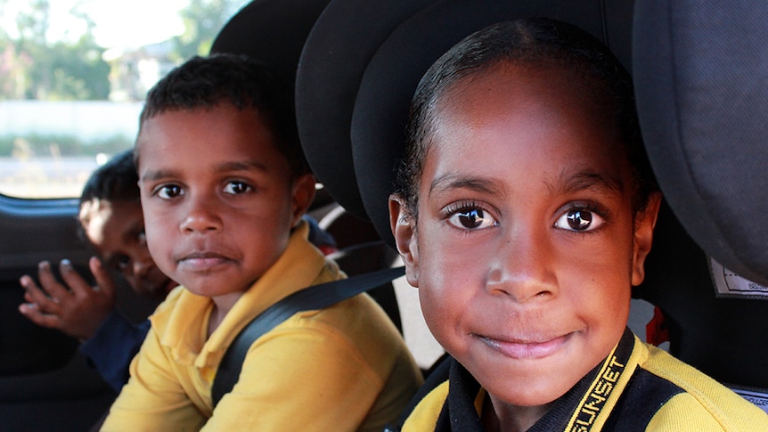 Two kids smiling at the camera while sitting in the bus.