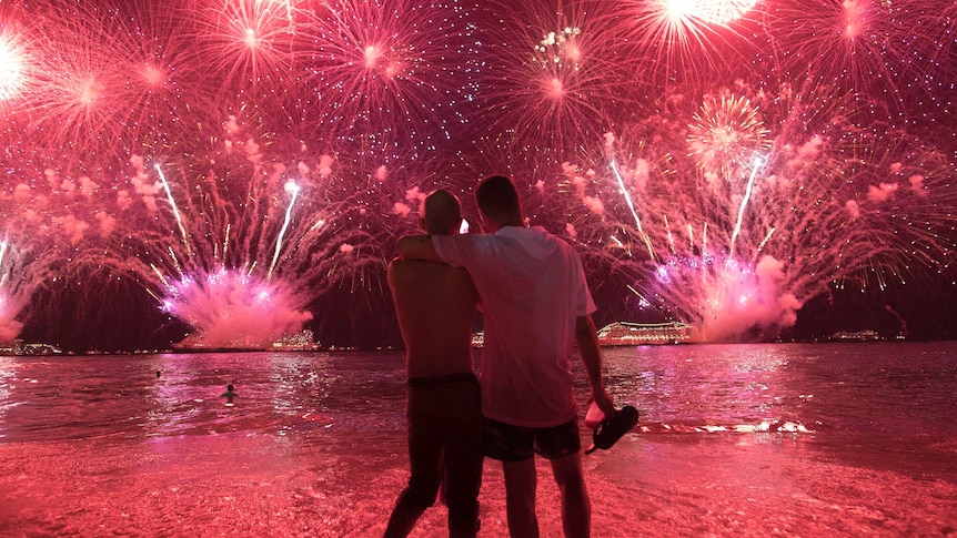 Two men watch the fireworks exploding in bright red over Copacabana Beach.