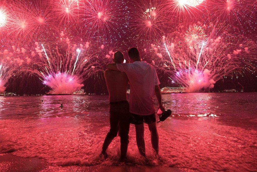 Two men watch the fireworks exploding in bright red over Copacabana Beach.