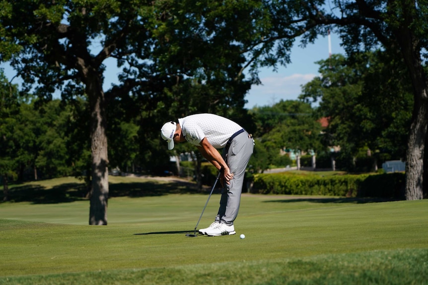 Collin Morikawa rests his hands on his knees and looks down at the ground