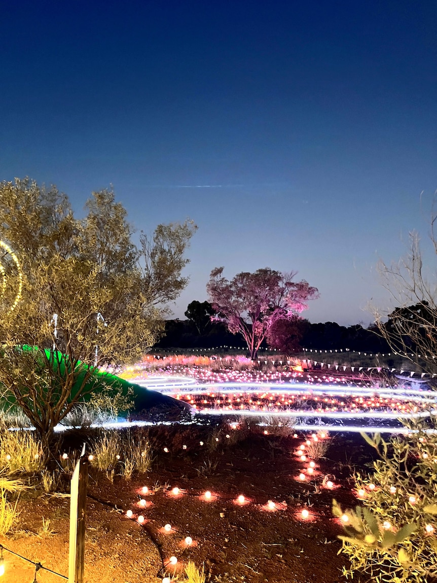 Fluorescent lights make artistic patterns on the dry, desert landscape at dusk.