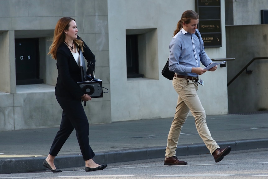 A woman in business attire crosses St Georges Terrace in Perth carrying a computer monitor next to a man carrying papers.