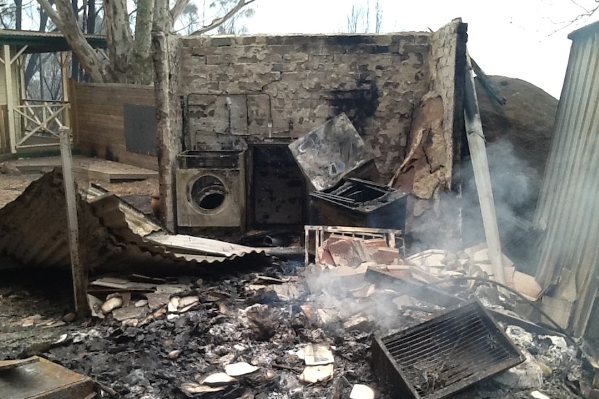 A burnt down laundry, without a roof and with mangled and burnt appliances.