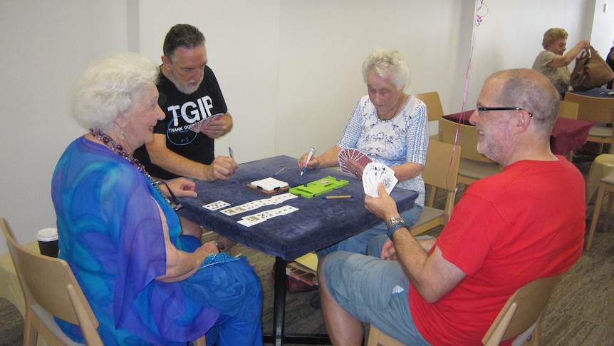 Four people sitting around a table playing a card game