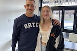 A woman with blonde hair and white shirt poses for a photo with a man wearing a navy blue jumper