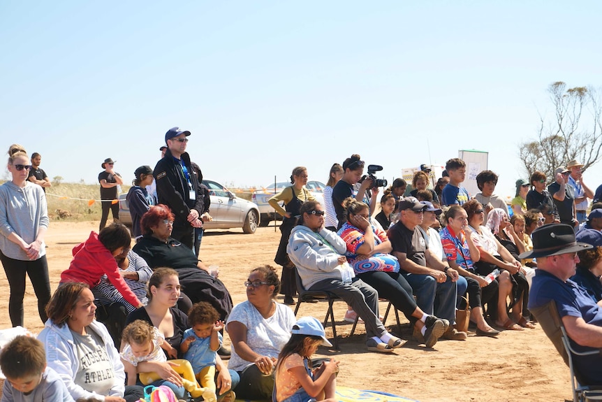 People sit on chairs and the ground under a blue sky