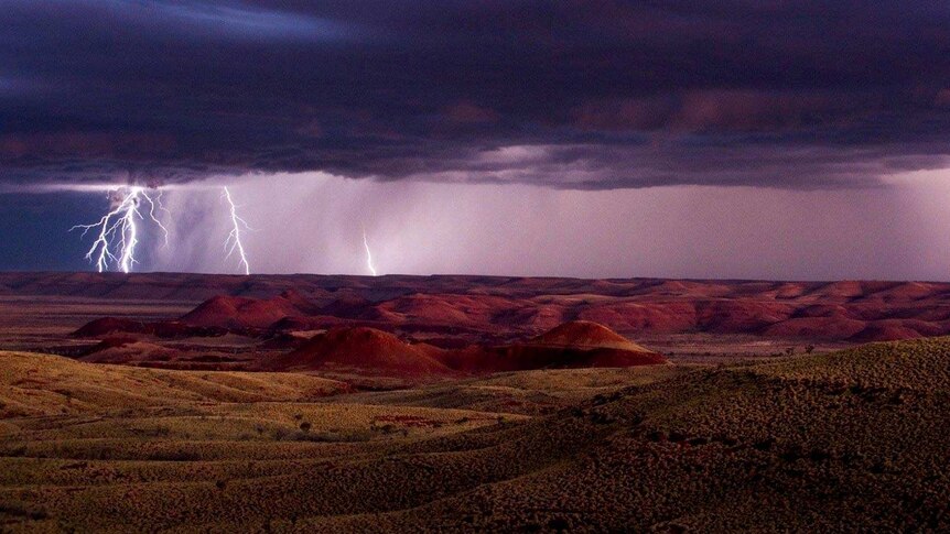 Elevated view across the vast outback landscape of bolts of lightning striking the ground at dusk.