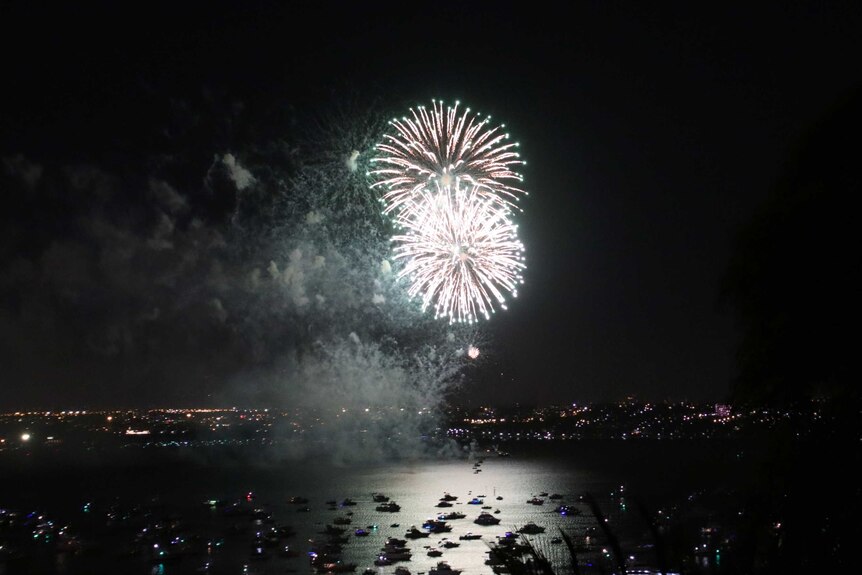 A wide shot of fireworks exploding over the Swan River in Perth, with boats on the water.