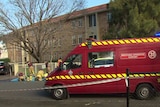 Firefighters gather near a red van that says "breathing apparatus support" outside a three-storey apartment building.