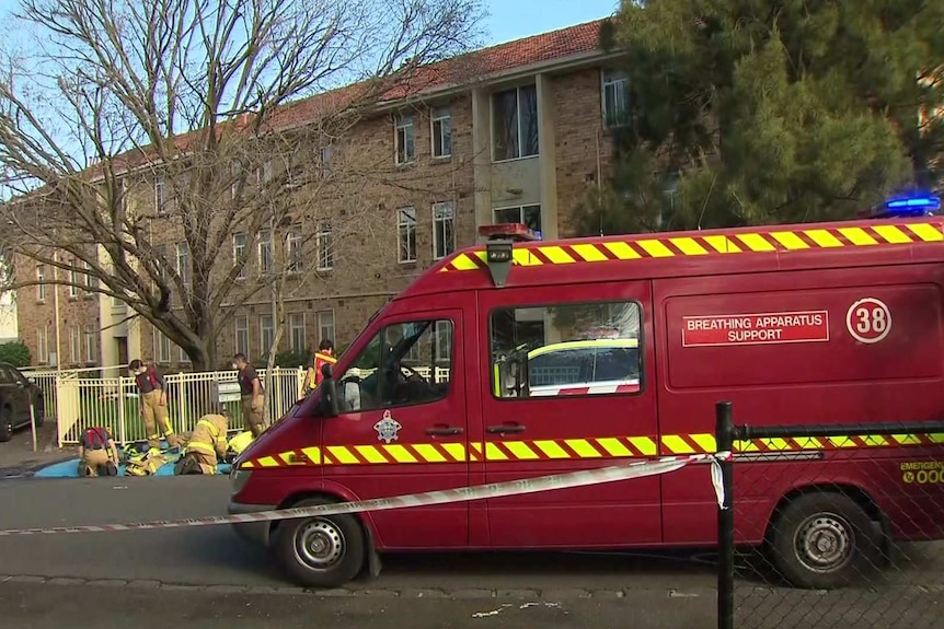 Firefighters gather near a red van that says "breathing apparatus support" outside a three-storey apartment building.