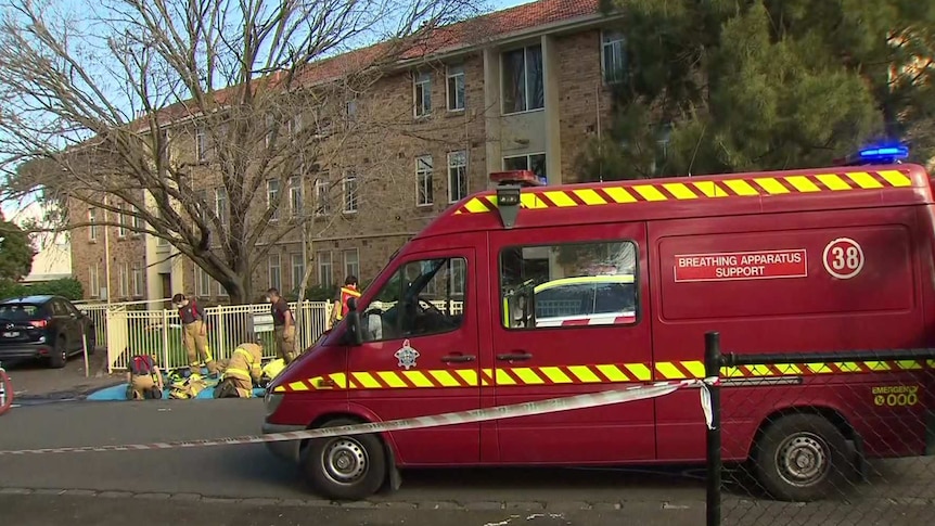 Firefighters gather near a red van that says "breathing apparatus support" outside a three-storey apartment building.