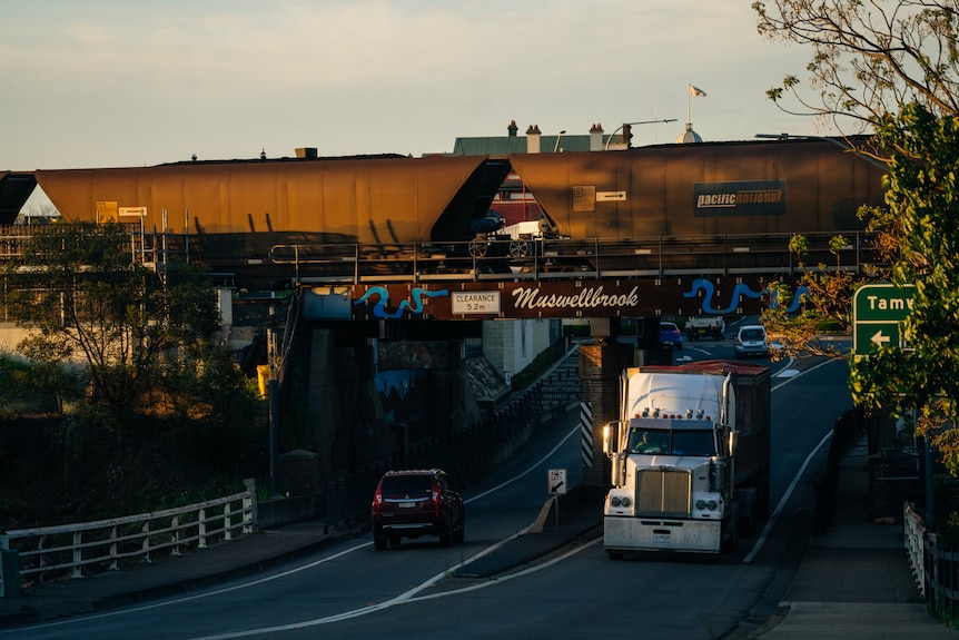 A coal train crossing a bridge with trucks driving underneath it.