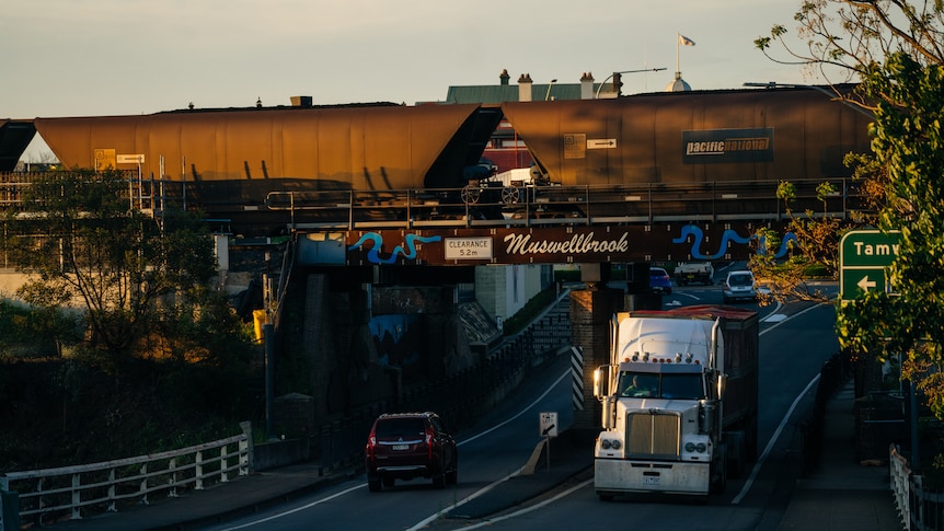A coal train driving over a bridge with trucks driving underneath.