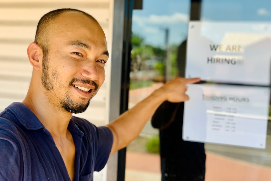 Un hombre sonríe mientras señala un cartel de 