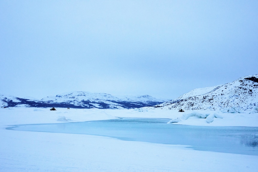 An icy landscape with hills and snow is pictured. On the ground is ice with a layer of water on top of it. 