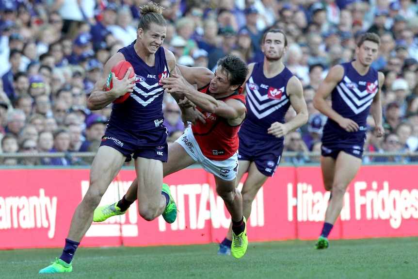 Fremantle Dockers captain Nat Fyfe brushes off a tackle from Essendon's Mark Baguley with two Dockers teammates behind him.