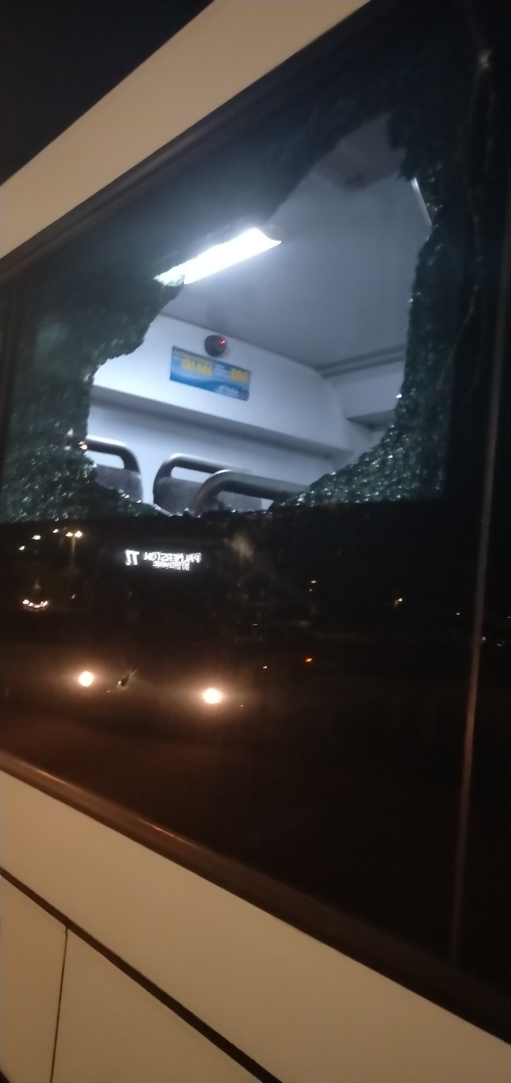 A large hole in the glass windscreen of a bus at night time. 