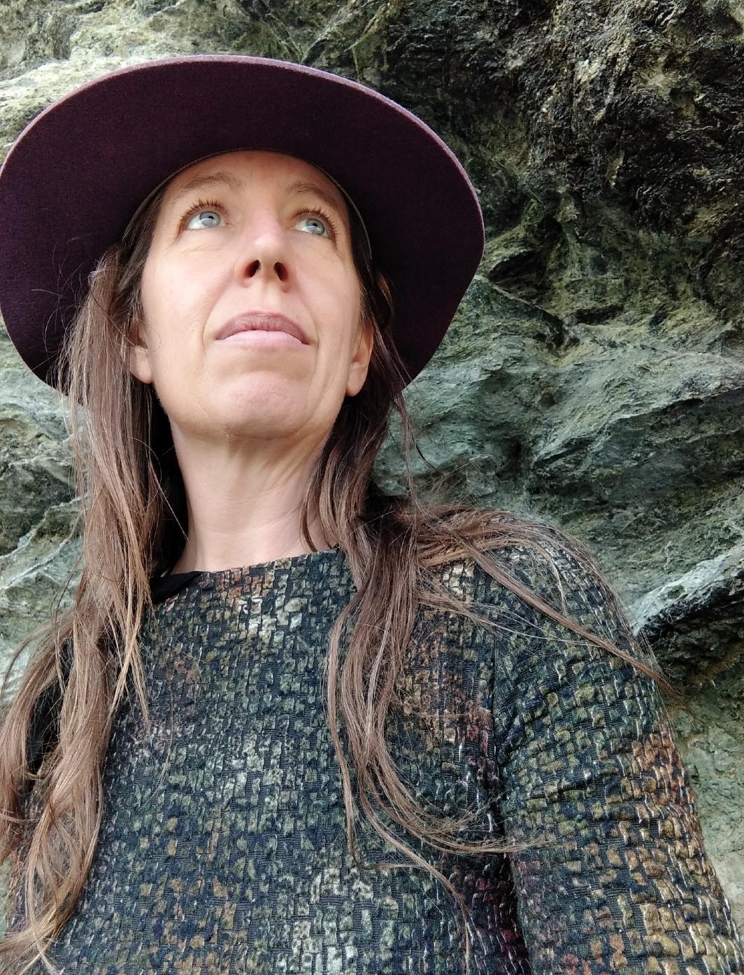 Portrait of a woman wearing felt broadbrimmed hat (low angle looking up) with a large beach rock behind her 