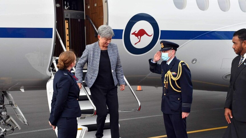 Penny Wong steps out of a plane onto a tarmac with three officials standing by.