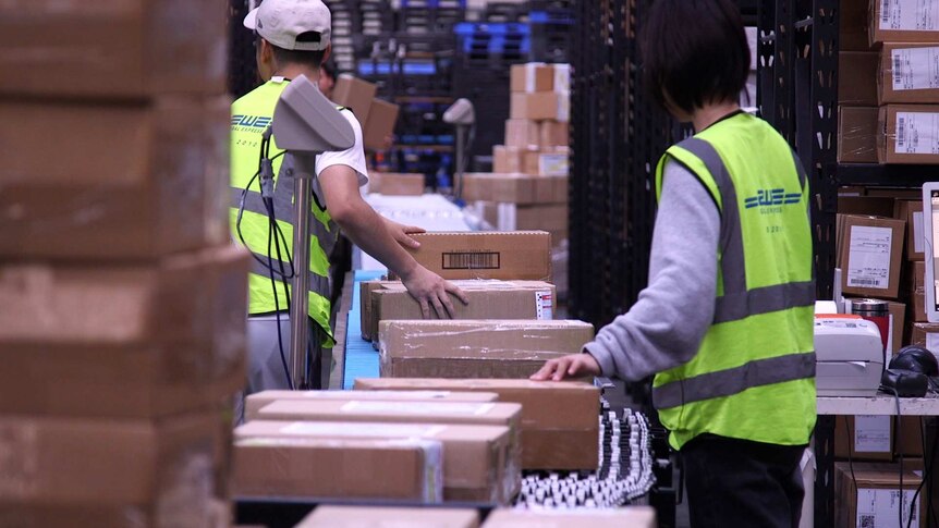 Workers place parcels on conveyer belts.