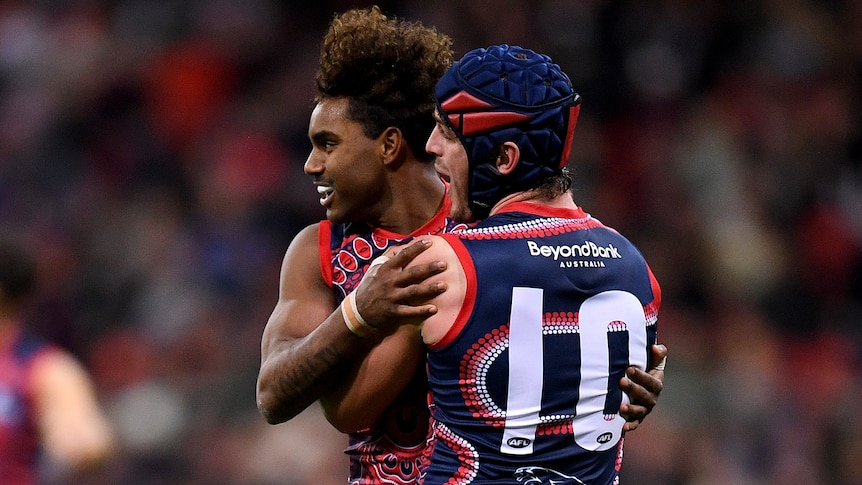 Two Melbourne AFL players embrace as they celebrate a goal against the Brisbane Lions.