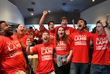 A group of people wearing ALP t-shirts sit around a table. Balloons are nearby.