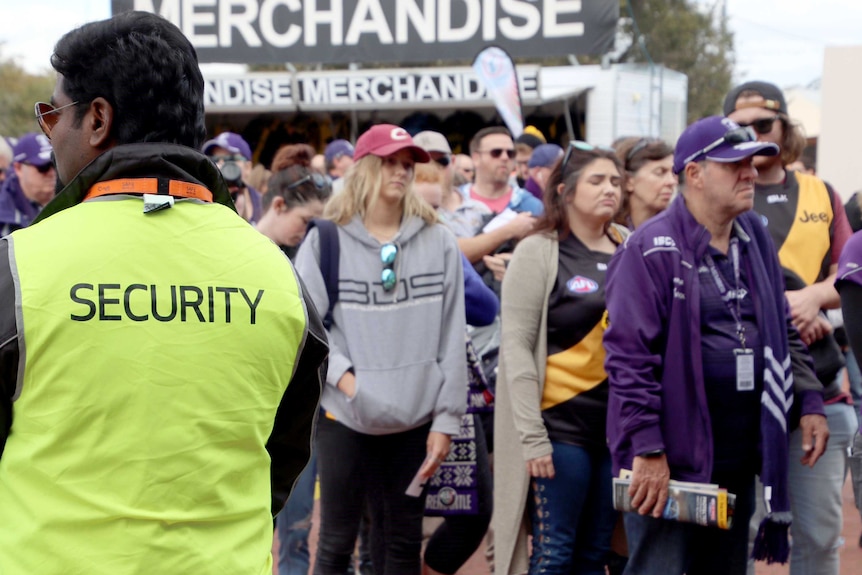 Crowds dressed in purple  line up as a Security guard watches.