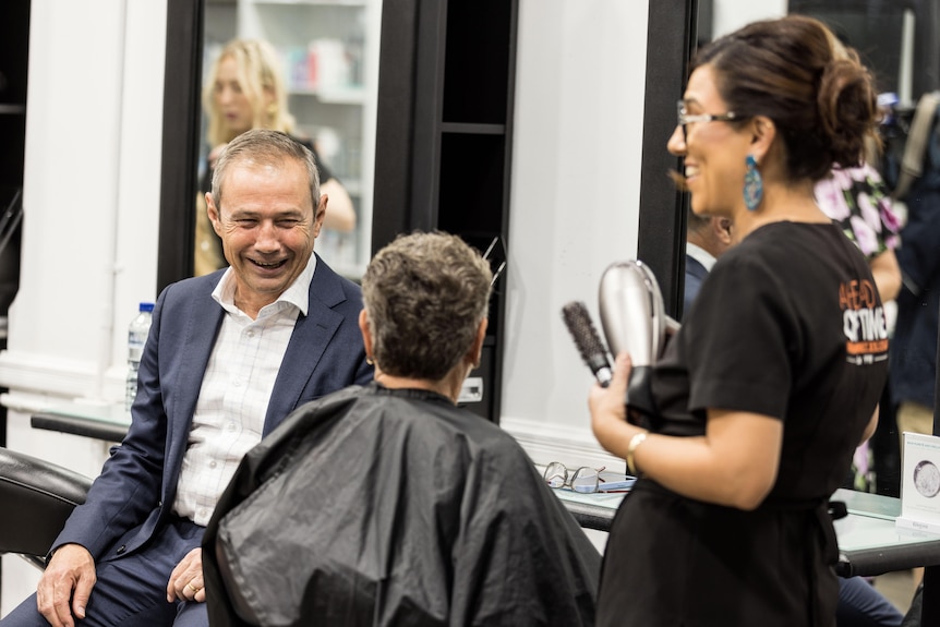 The Premier speaking to a woman getting her hair cut and a hair stylist.  