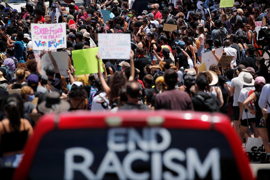 A crowd of people holding up signs, some with hands in the air.