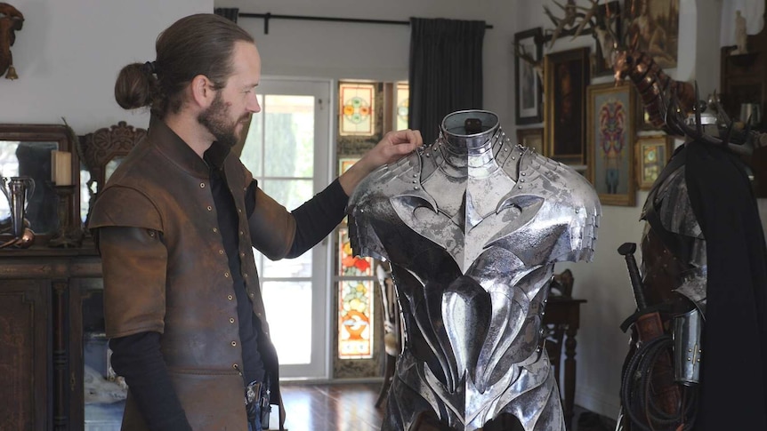 Man stands next a suit of armour