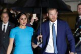 Prince Harry and Meghan, the Duke and Duchess of Sussex walk side by side holding an umbrella.
