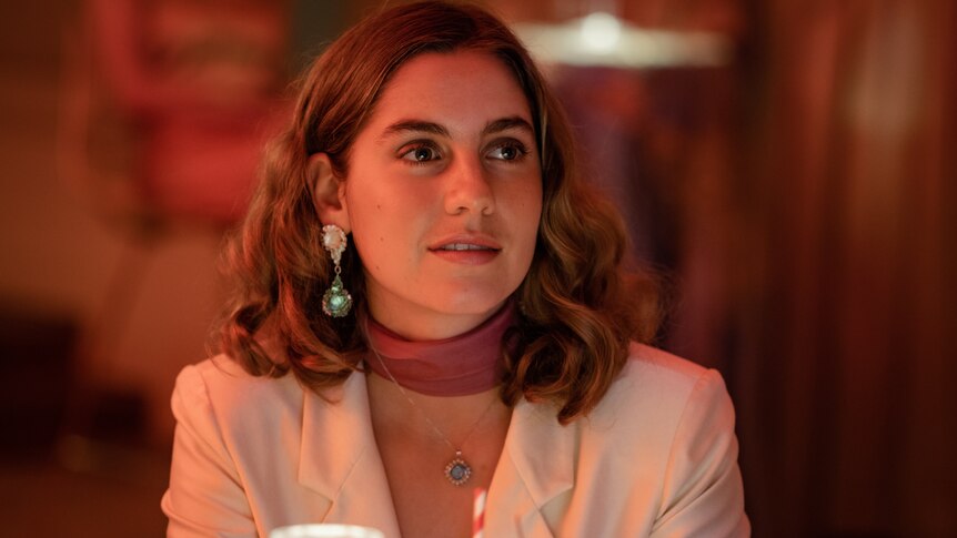 A 25-year-old woman with brown shoulder-length hair, large earring and formal clothes, sitting in a restaurant 