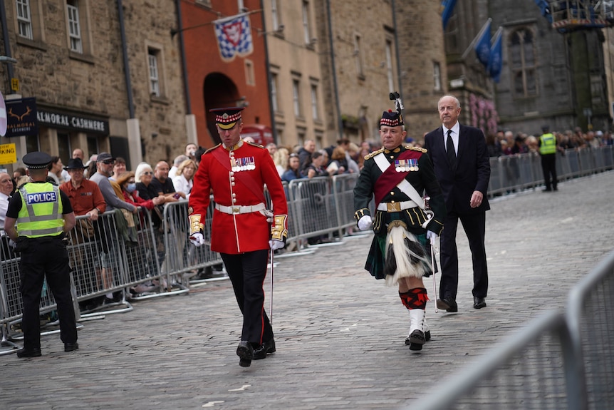 Two men in ceremonial uniform walk down a cobbled street.