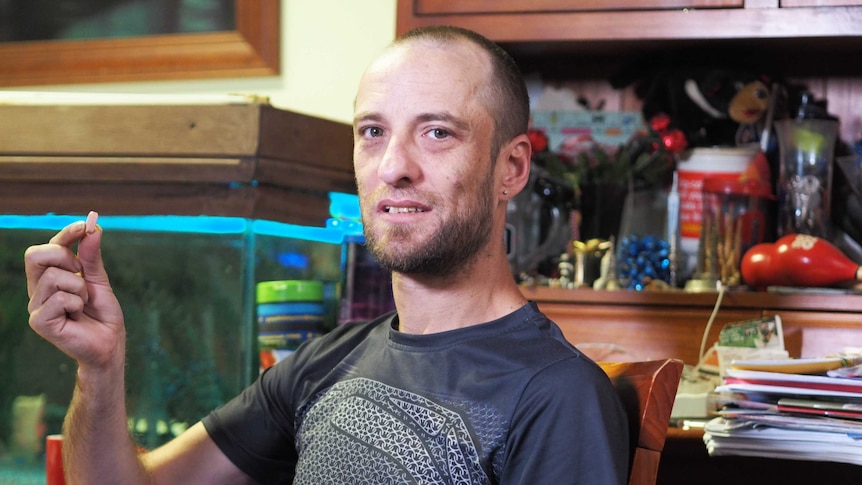 Adelaide resident Hayden Patterson holds up a large pill he takes to treat HIV.