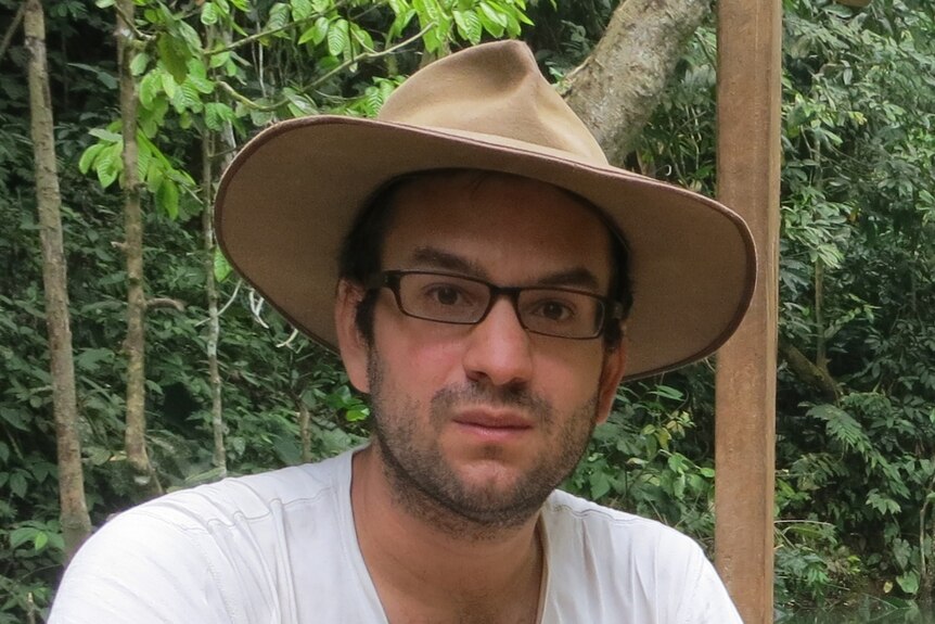 A man wearing glasses and an akubra hat looks at the camera