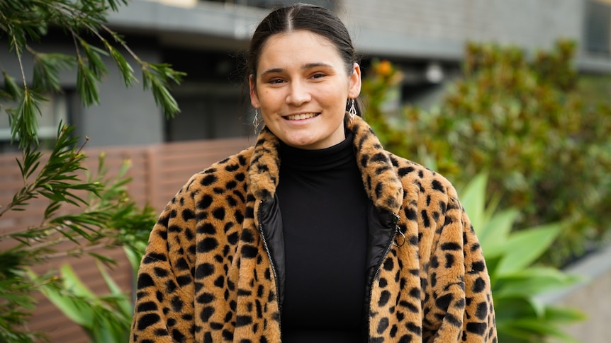 Molli Johns standing in front of the camera, smiling, wearing a black top and a leopard print jacket. 