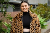 Molli Johns standing in front of the camera, smiling, wearing a black top and a leopard print jacket. 