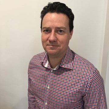 RMIT's Dr Warren Staples wears a check shirt and stands against a white background.