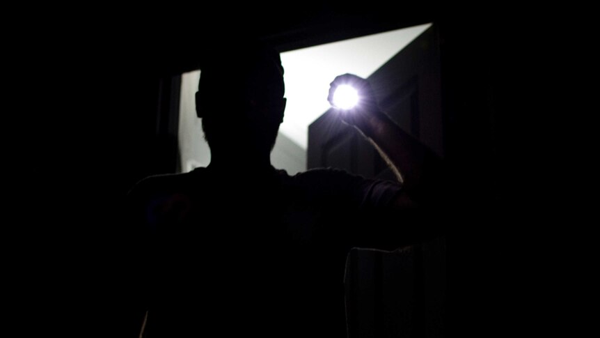 A silhouette of a man is seen as he shines a torch into the camera.