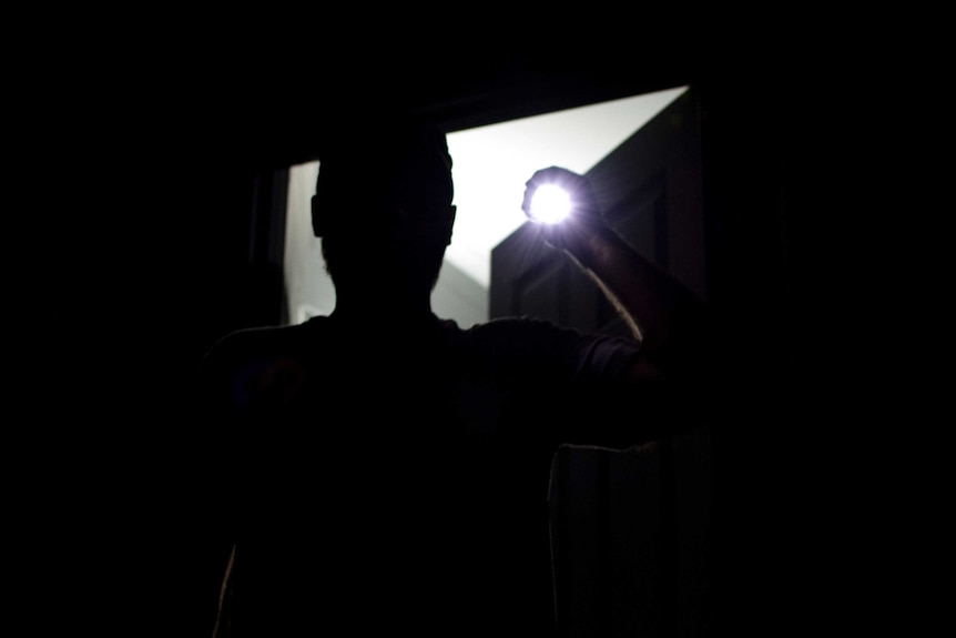 A silhouette of a man is seen as he shines a torch into the camera.