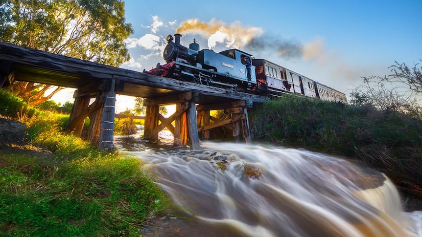 Steam train crosses wooden bridge with flooding below