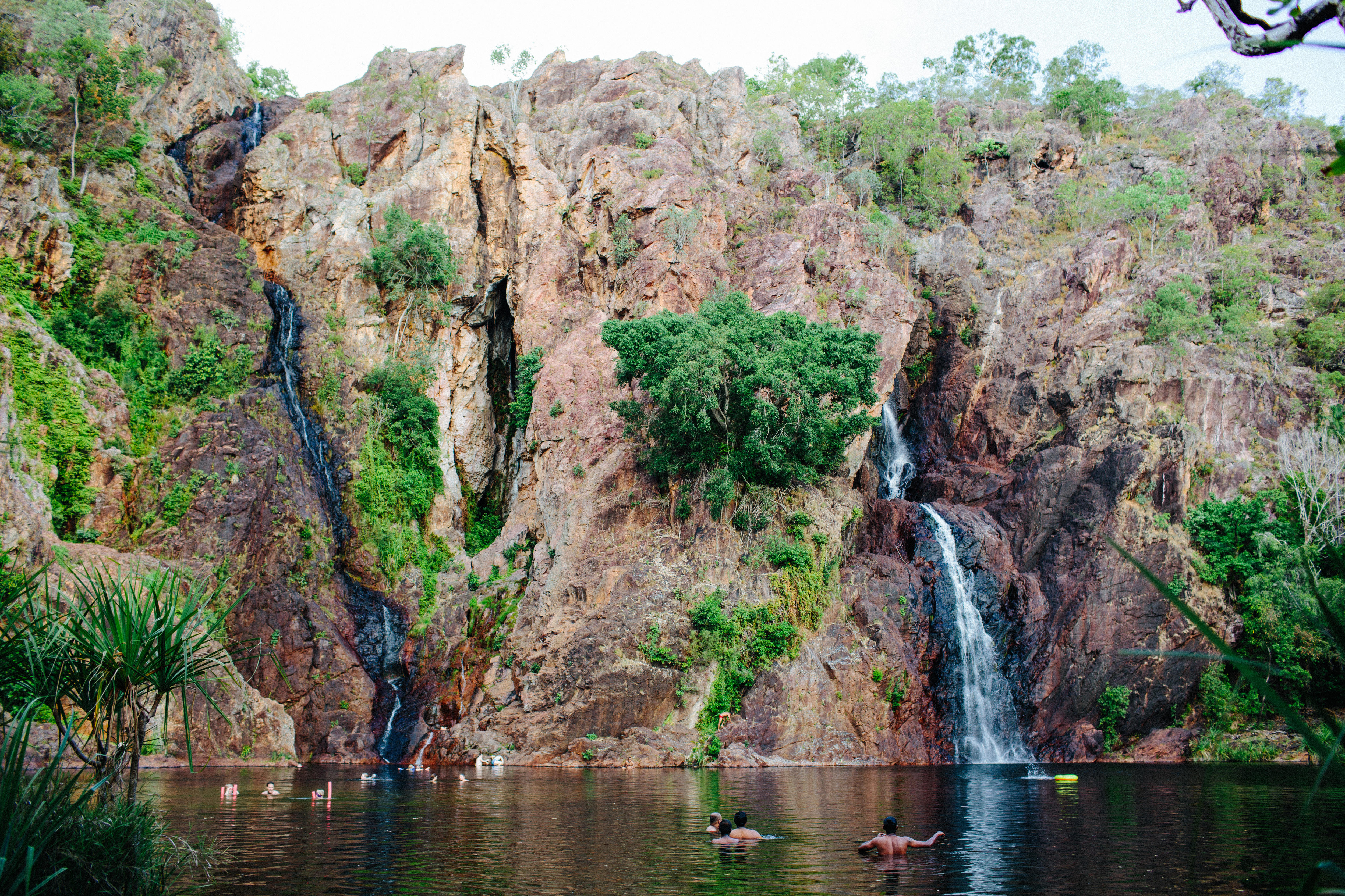 Banhistas nadam ao pé de uma grande cachoeira rochosa