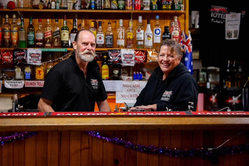 Man and a woman stand behind the bar inside the Flowerdale Hotel.
