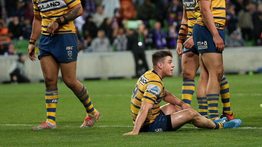 A group of Parramatta Eels players stand around looking on as Reed Mahoney sits on the ground and contemplates defeat