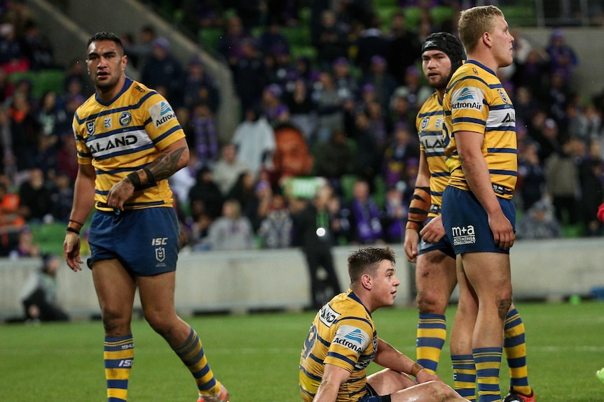 A group of Parramatta Eels players stand around looking on as Reed Mahoney sits on the ground and contemplates defeat