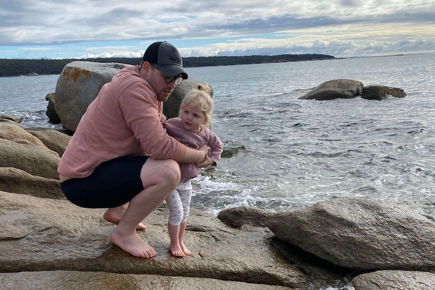 Man bending down holding onto a little girl by the ocean