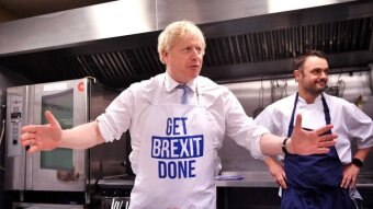 A man in a 'Get Brexit done' apron stands in a kitchen