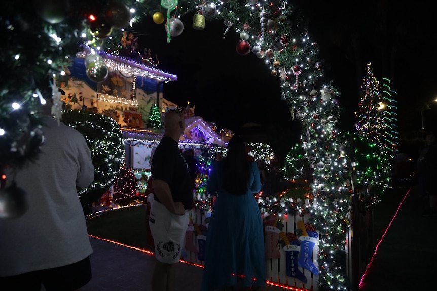 a crowd of people looking at a house covered in Christmas lights